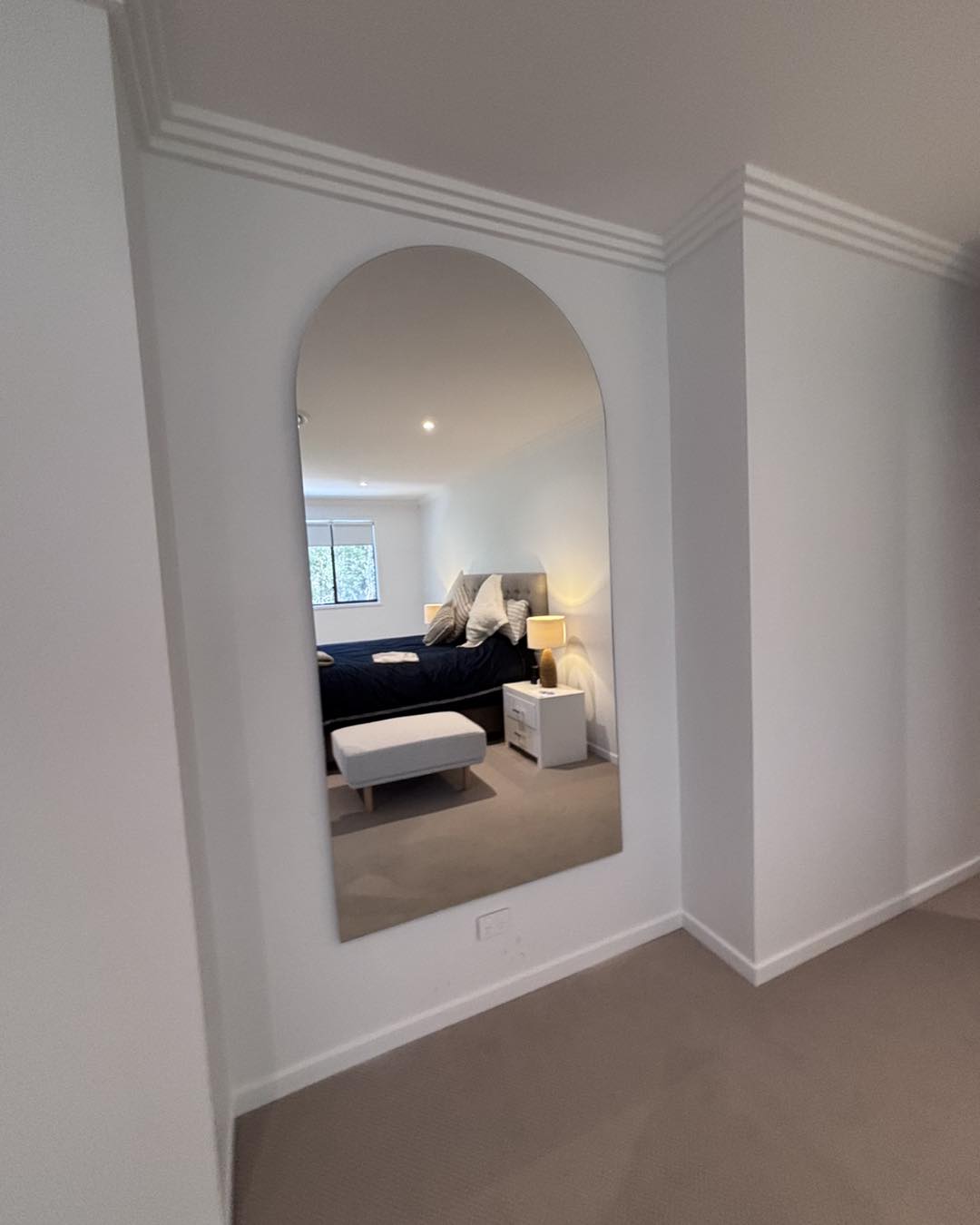 After: a large arched mirror hung flush on the wall, the bedroom reflected in it
